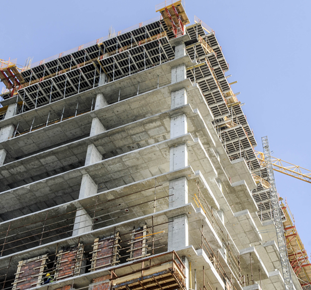 A concrete building under construction with scaffolding, support beams, and a crane in the background, representing infrastructure developmen.